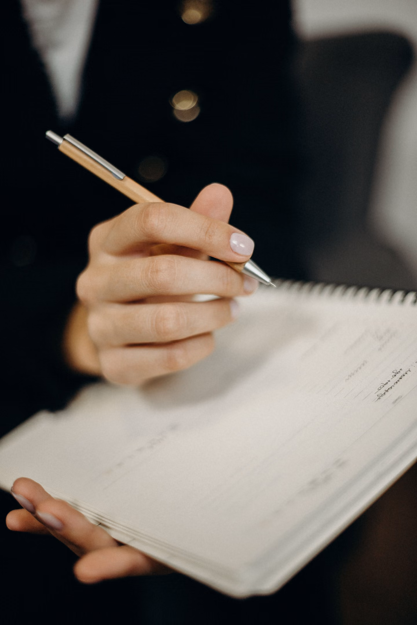 A hand writing names in a lined notebook with a pen, close-up.