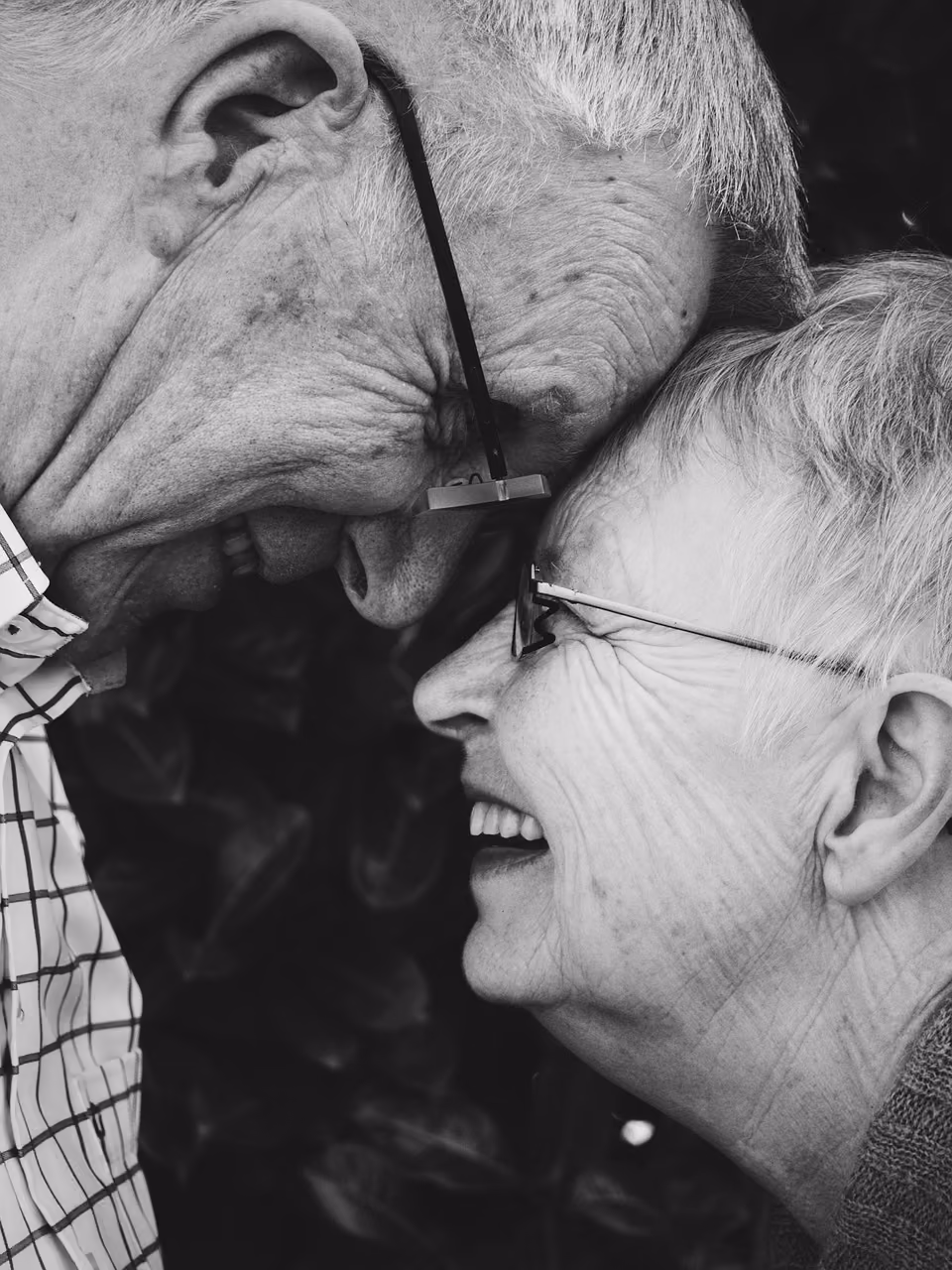 An older man and woman laughing together, in black and white, close up.