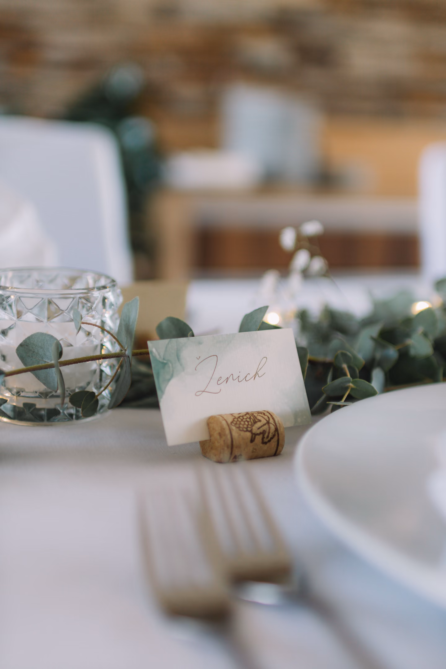 A wedding table setting with a folded napkin, cutlery and a handwritten name card on a plate.