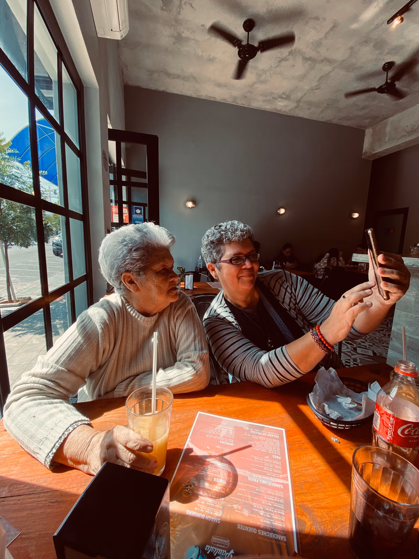 Two older people at a restaurant table looking at a phone together and laughing.